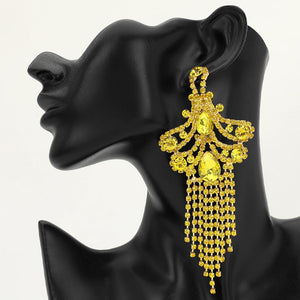 A woman wearing a large ornate yellow crystal statement earring with cascading bead fringe and yellow crystal accents against a light gray background.
