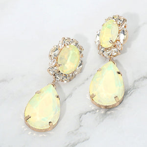 Yellow crystal oval and teardrop dangle earrings on gold on a white marble background
