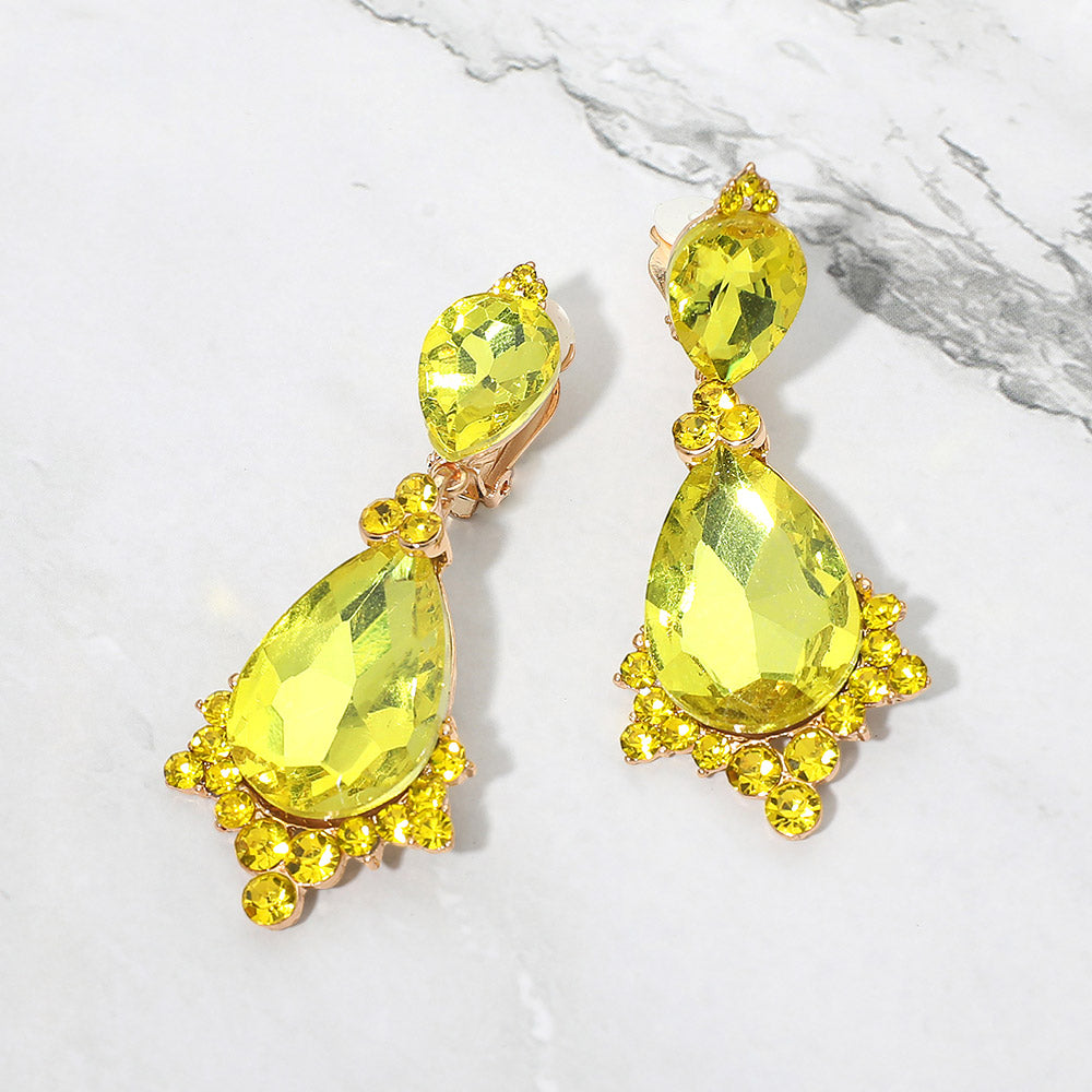 Yellow faceted teardrop clip-on statement earrings on gold on a white marble background