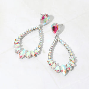 Iridescent AB crystal open teardrop dangle earrings on silver-tone settings, measuring 1.25 inches wide by 2.6 inches long. Stones reflect pink, blue, yellow, and green highlights. Faceted teardrop tops connect to open drops edged with small round crystals and larger teardrop and marquise-shaped stones along the bottom, displayed on white marble.