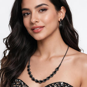 A model wears the black crystal version of this marquise necklace set on silver-tone settings with matching drop earrings and a black strapless dress. Leaf-shaped crystal clusters form a slim decorative line across the neckline. This same-style photo shows how the necklace and earrings sit when worn, against a light gray background.