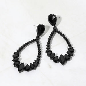 Black crystal open teardrop dangle earrings on black metal settings, measuring 1.25 inches wide by 2.6 inches long. Faceted teardrop tops connect to open drops edged with small round crystals and larger teardrop and marquise-shaped stones along the bottom, displayed on white marble.