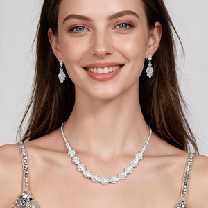 A model wears a clear crystal marquise necklace set on silver-tone settings with matching drop earrings and a silver embellished dress. Leaf-shaped crystal clusters form a slim decorative line across the neckline. The necklace measures 16 inches plus a 4-inch extender, with 0.4-inch decor; earrings are 0.9 inches long. Shown against a light gray background.
