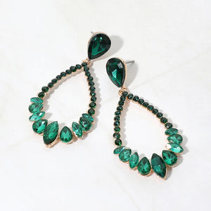 Emerald green crystal open teardrop dangle earrings on gold-tone settings, measuring 1.25 inches wide by 2.6 inches long. Faceted teardrop tops connect to open drops edged with small round crystals and larger teardrop and marquise-shaped stones along the bottom, displayed on white marble.