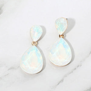 White opal crystal double teardrop dangle earrings on gold displayed on a white marble background.