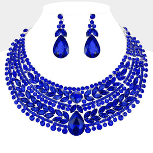 Sapphire royal blue crystal statement necklace set on silver-tone metal, featuring a broad, layered bib of marquise and round stones with a large teardrop centerpiece and matching teardrop earrings. Necklace measures 17 inches plus a 2-inch extender, with 2.25-inch decor; earrings are 2.2 inches long. Displayed on a white jewelry bust against a white background.