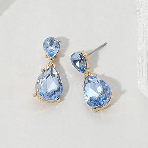 Double teardrop dangle earrings with light blue crystals on gold, measuring 1 inch long by 0.4 inch wide, featuring smaller faceted teardrops above larger drops, displayed on a white textured surface.