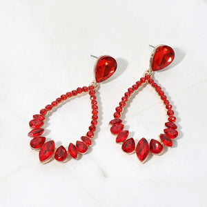 Red crystal open teardrop dangle earrings on gold-tone settings, measuring 1.25 inches wide by 2.6 inches long. Faceted teardrop tops connect to open drops edged with small round crystals and larger teardrop and marquise-shaped stones along the bottom, displayed on white marble.